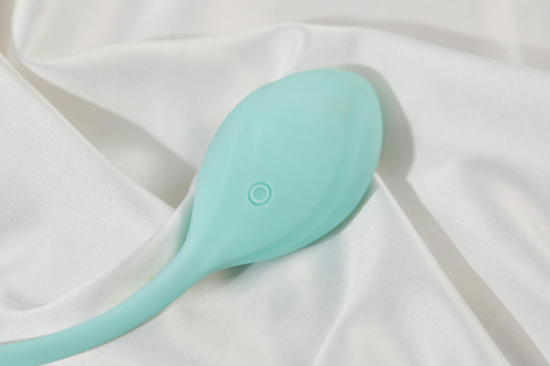 A sleek teal lemon vibrator on smooth white silk fabric, showcasing modern intimate wellness design